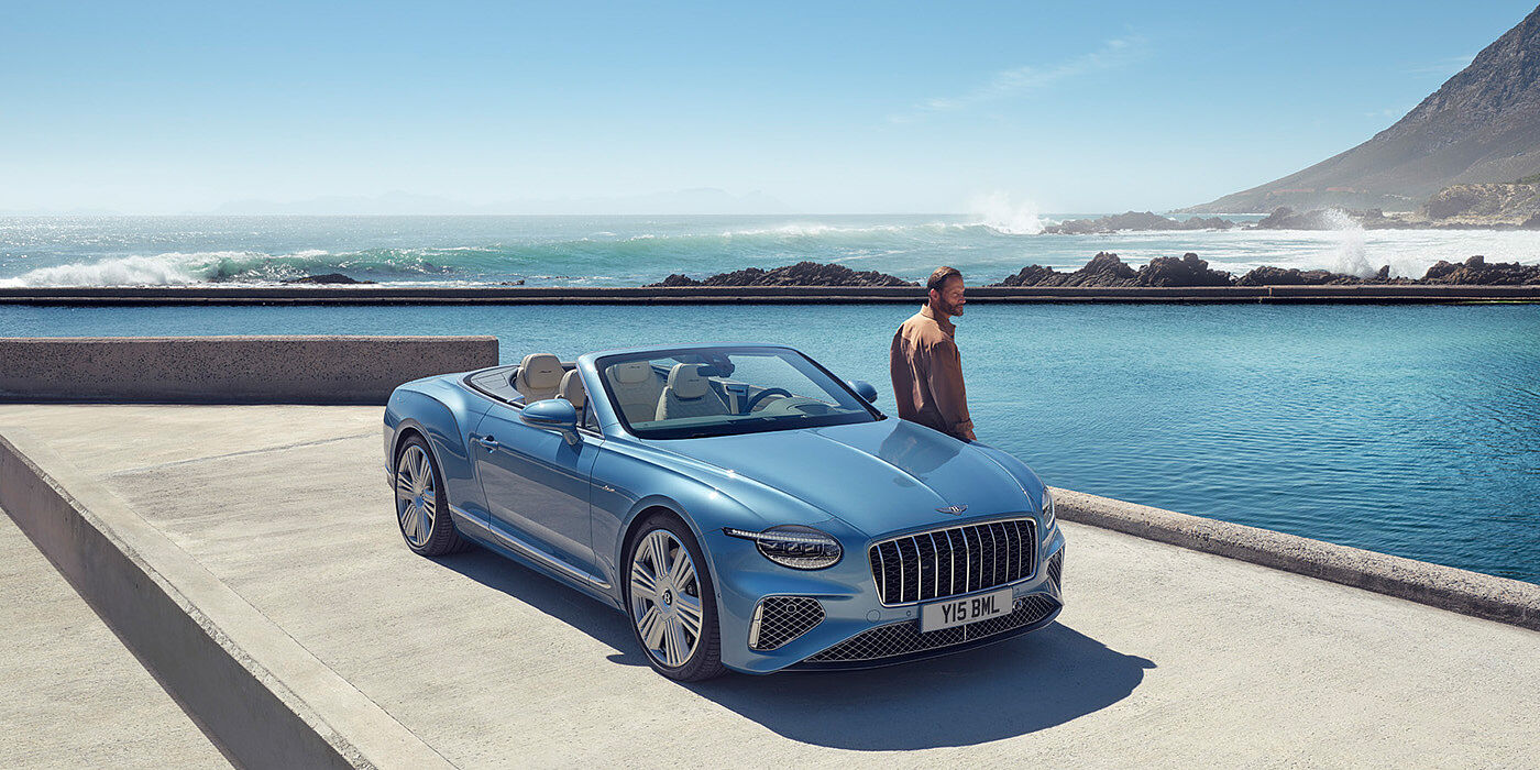 Bentley New Delhi New Bentley Continental GTC Azure convertible front view in Light Windsor blue paint with 22 inch ten spoke wheels parked by the sea in the sunshine
