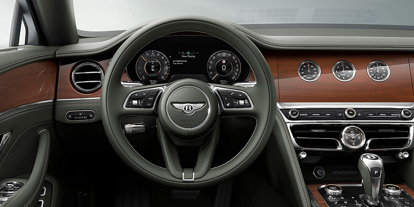 Bentley New Delhi New Bentley Flying Spur sedan front cabin in Cumbrian Green hide and Crown Cut walnut veneer showing steering wheel and Rotating Display with three clocks on face