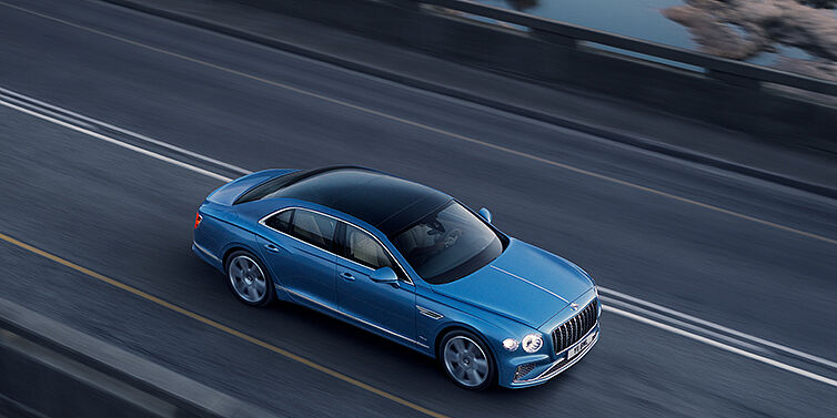 Bentley New Delhi New Bentley Flying Spur Azure sedan in Light windsor blue paint by Mulliner, with 22 inch Azure wheels seen from overhead driving dynamically on a country road